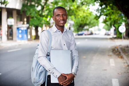 young man standing in street with laptop looking at the camera smiling.の写真素材