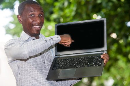 young man standing in shirt with laptop watching the camera laughing.
