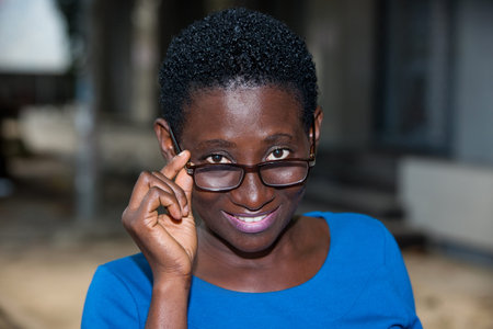 young girl standing in blue camisole eyeglasses looking at camera smiling.
