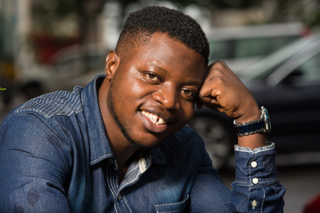young african man sitting in jeans shirt looking at camera smiling.