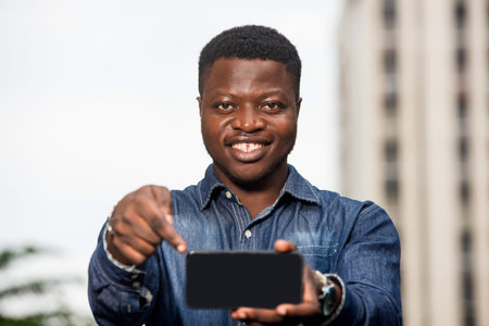 young man standing in jeans with mobile phone looking at camera laughing.