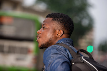 young man standing in jeans with backpack looking at mobile phone while smiling.