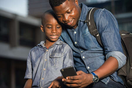 Father and son sitting in the street waiting for a car, look together on a mobile phone. concept of tourist and travel with children.の写真素材