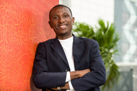 young african man standing in arms crossed suit looking at camera smiling.