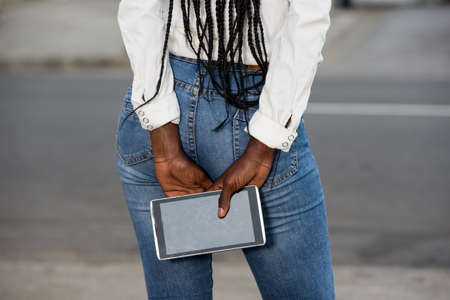 young woman in casual outfit standing back, showing showing of smart phoneの写真素材