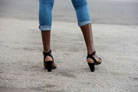 fashion and make-up concept, close-up of woman legs in jeans and black heels on a road in daylightの写真素材