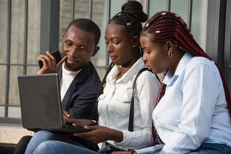 Group of young people using smart computers outdoors in urban context. Women and men sitting on the...