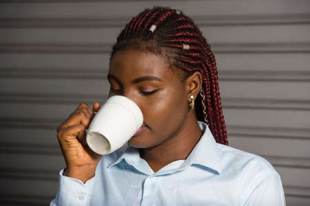Young girl with a cup of coffee stands on the street next to the business center. Businesswoman drinks hot and invigorating drink at night after workの写真素材