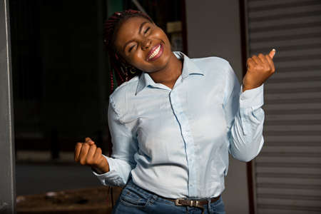 young african girl standing in blue shirt looking at the camera smiling with closed fists.の写真素材