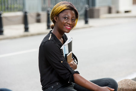 happy university student sitting alone outdoors holding books
