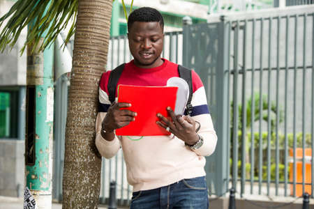 young student standing near coconut tree looking at notebook smiling.の写真素材