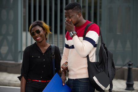 Happy female students with positive expression hold hands, carry backpacks, make friendly speeches,...