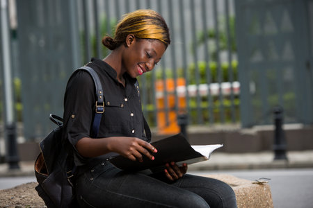 Beautiful college girl reading and writing notes in notebook in campus park.