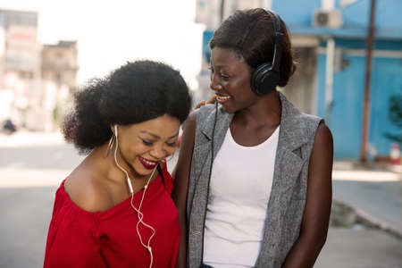 Two beautiful and happy young women are smiling, talking and looking for something on a cell phone in the cityの写真素材