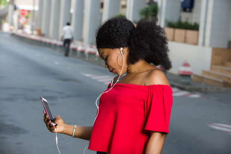 Portrait of beautiful girl with long hair and holding smart phone and wearing headphones laughing at the funny video she is looking at online. Technology conceptの写真素材