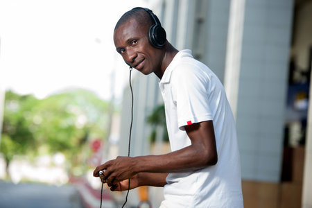 people, music, technology, leisure and lifestyle - Happy african young man with headphones and smart...
