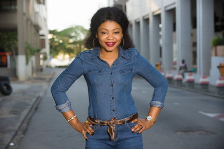 Young happy and free woman standing on the street posing with her hand on her hip and looking at the...