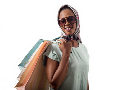 young girl isolated on white background in sunglasses head scarf and shopping bags on the shoulder look in profile while smiling.の写真素材