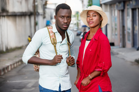 young couple of tourists standing in the street in jeans backpacks watching the camera smiling.