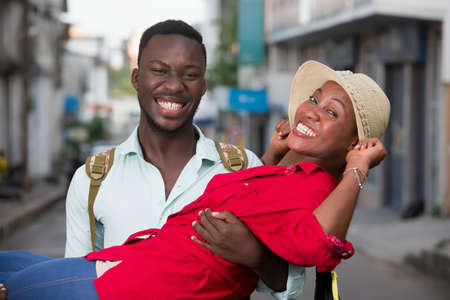 young man walking down the street holding his daughter friend in his arms laughing.の写真素材