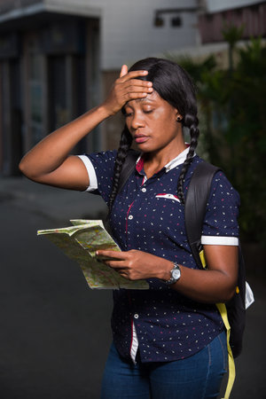 young female tourist standing in street backpack looking at map with hand on forehead.