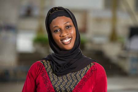 young muslim woman standing outdoors looking at camera smiling.