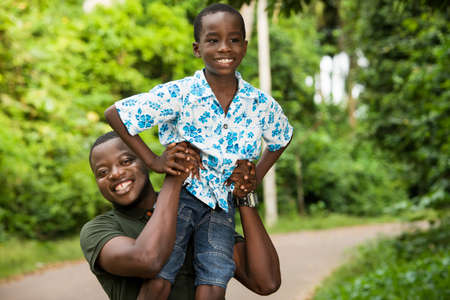 a young man standing in a park with his son on the shoulder smiling.の写真素材