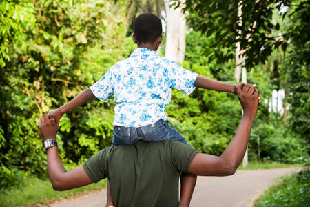 a young man standing in a park with his son on his neck giving back to the camera.の写真素材