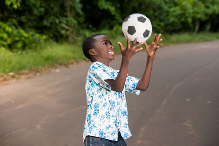 young boy standing outdoors playing ball with a smile.の写真素材