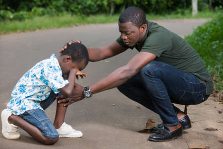 a young man crouched in a park air to calm his son who is crying.の写真素材