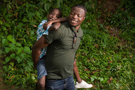 a young man kneeling in a park with his child on his back smiling.の写真素材