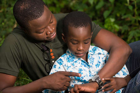 a young man lying in a park watching his watch with his child smiling.の写真素材