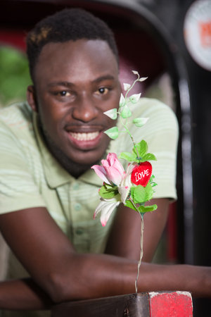 young man in tee-shirt with elbows on a chair looking at a flower while smiling.の写真素材