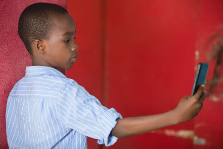 young boy standing in shirt in a studio looking at mobile phone.の写真素材