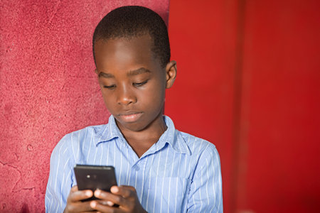 young boy standing in shirt in a studio looking at mobile phone.