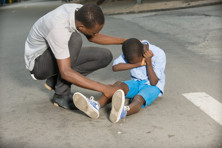 Father comforting his son crying, child fallen on the road having a knee injuryの写真素材