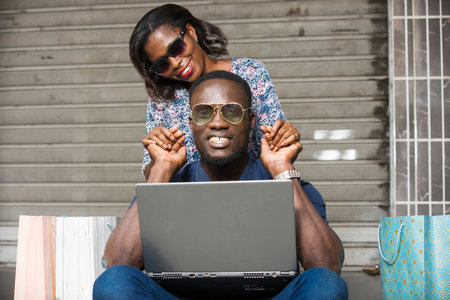 Happy couple using a laptop sitting outside and spending time together after doing a shoppingの写真素材