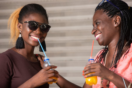 young girls standing in sunglasses drinking fruit juice while laughing.の写真素材