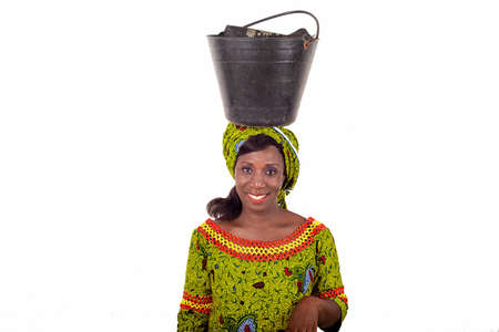 beautiful African adult woman dressed in green loincloth balances a black bucket on her head and accompanied by a beautiful smileの写真素材