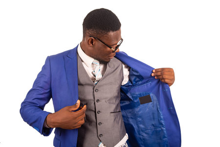 Handsome young businessman wearing glasses looking inside his blue jacket. isolated on white...