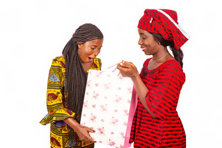Two beautiful african women standing in traditional outfit looking in bags of surprise shopping.の写真素材