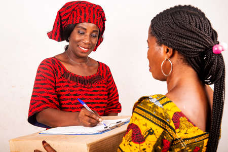 beautiful african woman standing in traditional dress on white background smiling signing a document after receiving an online package.の写真素材
