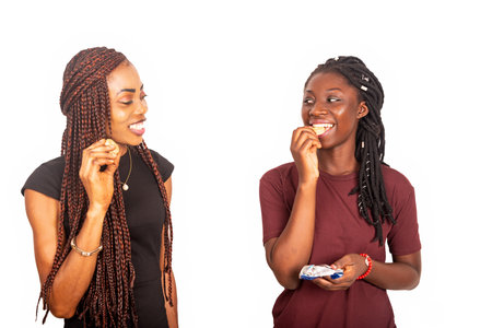 happy young beautiful girlfriends standing while eating cookies while being smilingの写真素材