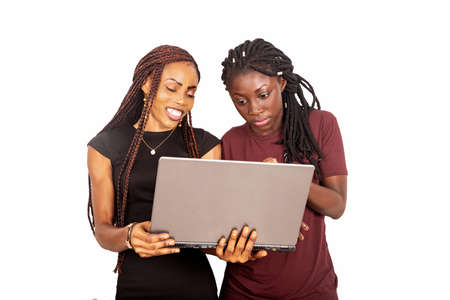 Two african young people standing perplexed in red and black clothes holding, and using a laptop while smiling isolated on white backgroundの写真素材