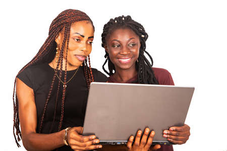 two young beautiful sisters standing in black and red colors holding and using a laptop while smilingの写真素材
