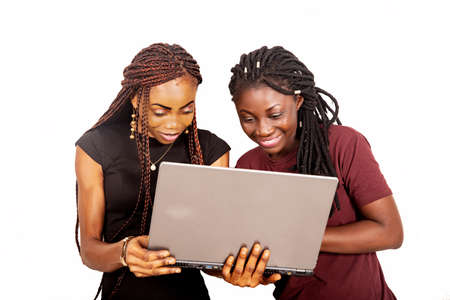two young beautiful sisters standing with a laptop while smilingの写真素材