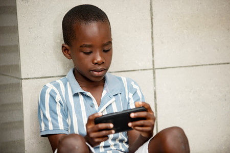 pretty little boy sitting playing games on the cell phone outdoors smilingの写真素材