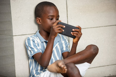 pretty little boy with serious hair sitting on the floor, feet crossed, holding the phone and...