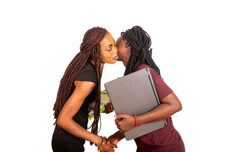 Two beautiful businesswomen standing on white background kissing each other while smiling holding laptop and documents.の写真素材