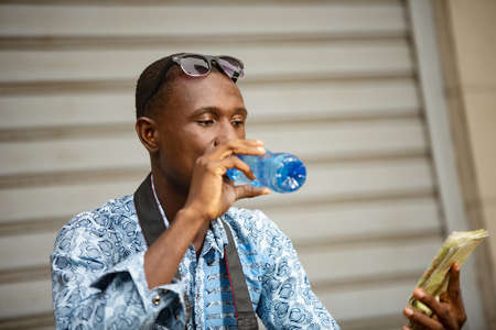 handsome young african photographer sitting outside holding a mobile phone and looking at camera smilingの写真素材